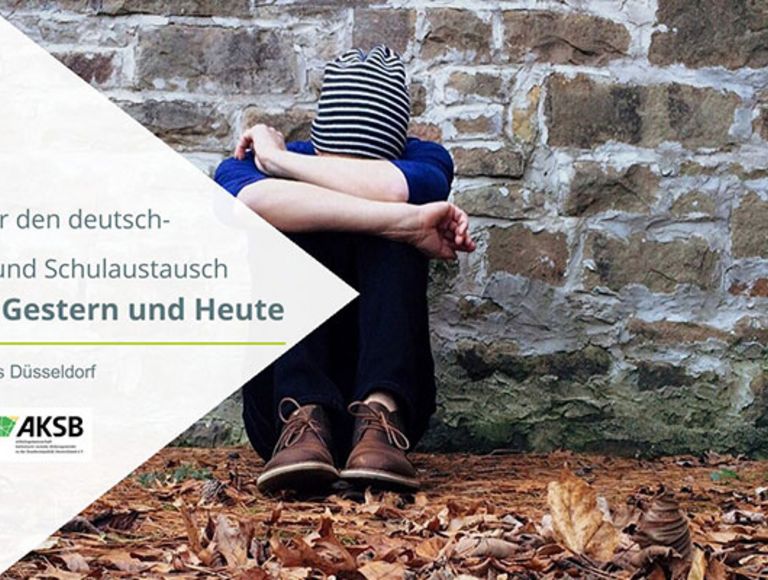 Junger Mensch zusammengekauert vor einer Mauer