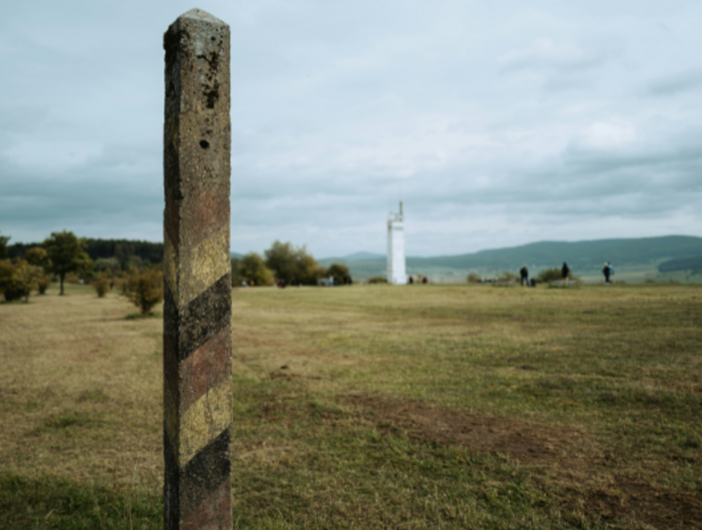Ein DDR-BRD-Grenzpfahl steht vor einem Wachturm in der Gedenkstätte Point Alpha