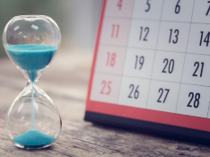 Durch eine Sanduhr rieselt Sand, dahinter steht ein Kalender.